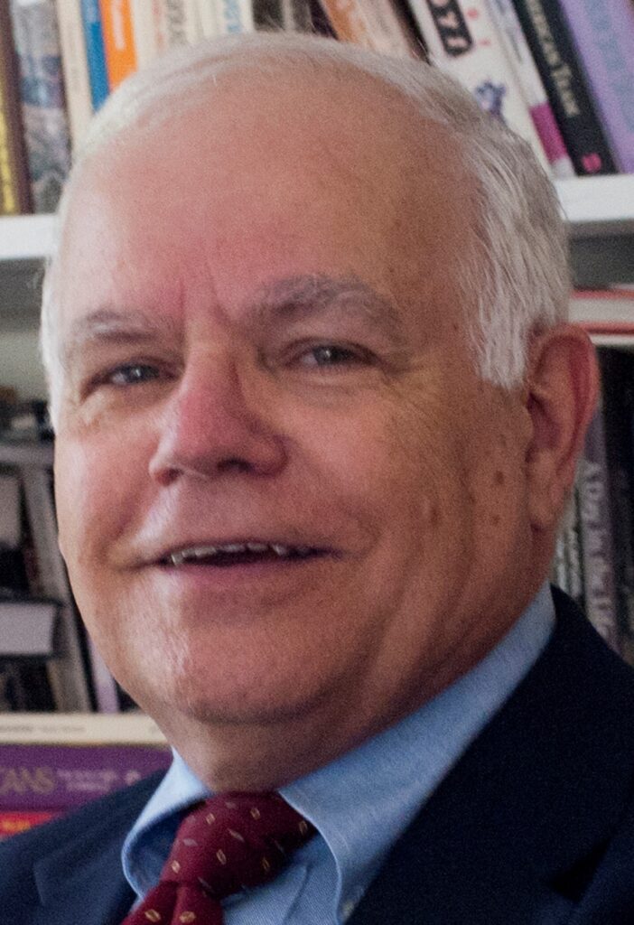 A white man with grey hair and blue eyes smiles warmly at the camera.