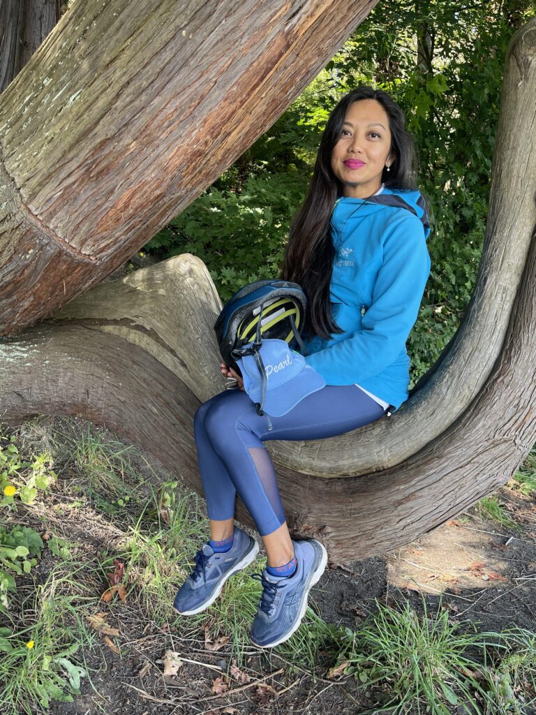 Photograph of author L. Ayu Saraswati. She is wearing blue activewear and sitting in a tree, surrounded by nature.